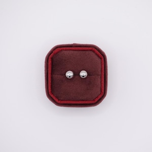 May include: A pair of silver ball stud earrings in a red velvet jewelry box.