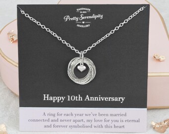 May include: Silver necklace with a pendant of ten intertwined rings and a small heart charm. The necklace is displayed on a black card with the text "Happy 10th Anniversary" and a message about the rings representing each year of marriage.