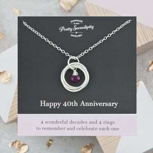 May include: Silver necklace with a pendant of four interlocking rings and a purple gemstone. The card reads "Happy 40th Anniversary" and "4 wonderful decades and 4 rings to remember and celebrate each one".