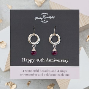 May include: A card with the text "Happy 40th Anniversary" and "4 wonderful decades and 4 rings to remember and celebrate each one". The card features a pair of silver and gold hoop earrings with a dangling red gemstone.