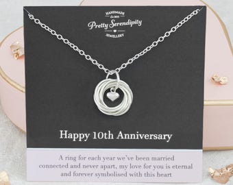 May include: Silver necklace with a heart charm and ten intertwined rings. The necklace comes on a black card with the text "Handmade Est 2015 Pretty Serendipity Jewellery Happy 10th Anniversary A ring for each year we've been married connected and never apart, my love for you is eternal and forever symbolised with this heart."