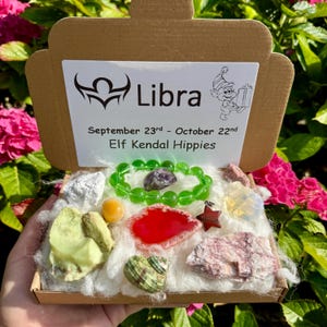 May include: A Libra gift box containing crystals and a green beaded bracelet. The box lid displays the Libra symbol, dates September 23rd - October 22nd, and the text "Elf Kendal Hippies". The box is open, revealing various gemstones and crystals.