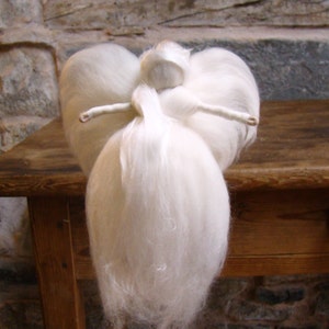 May include: A handmade white angel figurine with outstretched arms. The angel has large, fluffy wings and a flowing gown. The figure is made of soft, white material, possibly wool or felt, and sits on a wooden surface.