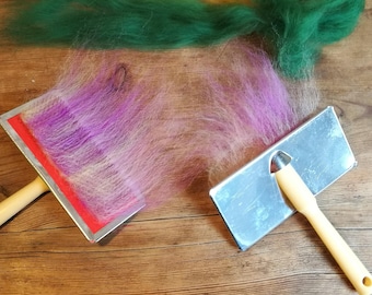 May include: Two felting tools with wooden handles. One tool has a red base and the other has a silver base. A strand of pink and purple wool is being felted on the red tool.