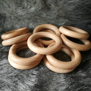 May include: A set of wooden rings, stacked and overlapping, with a natural wood finish. The rings are smooth and have a slightly rounded edge. They are arranged on a fuzzy, grey surface.