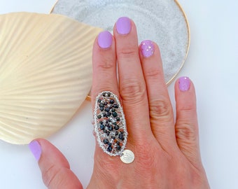 Puede incluir: Un anillo de plata con cuentas negras y un pequeño dije de plata. El anillo está en un dedo con esmalte de uñas morado.