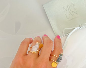 Puede incluir: Dos anillos de oro con delicados diseños de alambre. Un anillo presenta un grupo de piedras blancas, mientras que el otro presenta un grupo de piedras gris oscuro. Ambos anillos tienen un pequeño dije de oro con la palabra "MILAN" y un diseño floral.