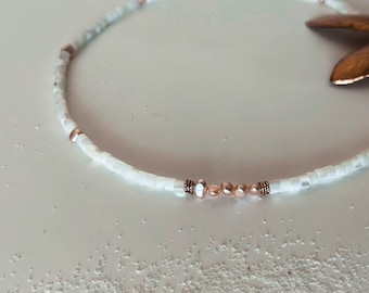 Puede incluir: Un collar de cuentas blancas con detalles en oro rosa. El collar presenta pequeñas cuentas blancas redondas y algunas cuentas más grandes de oro rosa.