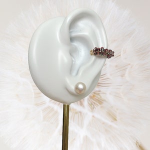 May include: A pair of earrings, one is a small pearl stud and the other is a gold hoop with a cluster of red and green beads.