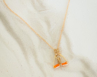 Puede incluir: Un collar de cadena dorada con un colgante con forma de mariposa. La mariposa está hecha de alambre dorado y tiene cuentas naranjas para sus alas.