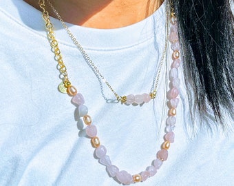 Puede incluir: Un collar de dos capas con una cadena de oro y una hebra de cuentas rosadas y doradas. Las cuentas tienen una forma irregular y un aspecto natural y pulido.