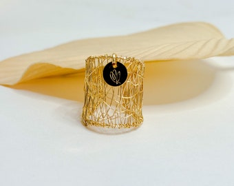 Puede incluir: Un anillo de alambre dorado con un pequeño dije redondo adjunto. El dije es negro y tiene un diseño floral.