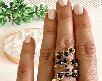 Puede incluir: Un anillo de oro con cuentas negras y un dije. El anillo se lleva en un dedo con esmalte de uñas rosa claro.