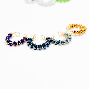 May include: Four wire-wrapped rings with different colored crystal beads. The rings are made with gold wire and feature blue, purple, teal, and gold beads.