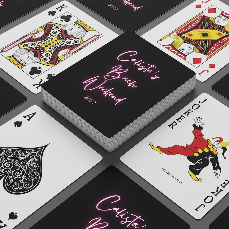May include: A stack of playing cards with a black background and white text that reads "Calista's Bach Weekend 2022". The top card is a King of Clubs, the bottom card is a Joker, and the cards in between are not visible.