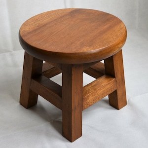 May include: A small, round wooden stool with four legs and a simple design. The stool is made of light brown wood and has a smooth, polished finish.