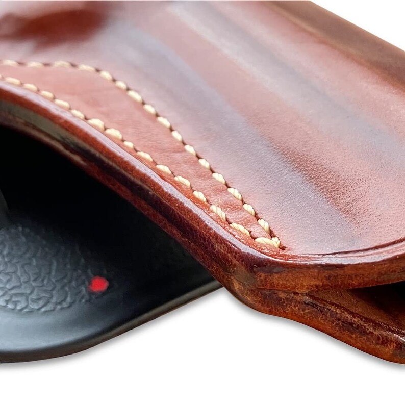 May include: Close-up of a brown leather holster with light brown stitching detail. The holster is folded in half, showing the inside of the holster.