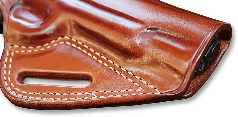 May include: A brown leather holster with white stitching. The holster has a belt loop and a cut-out for a gun.