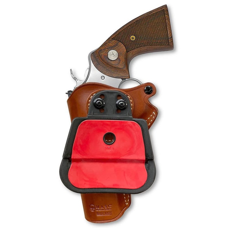 May include: A brown leather holster with a black plastic clip and a red rubber insert. The holster is designed to hold a revolver with a wooden handle. The holster is labeled "MASC" and "Hand Made".