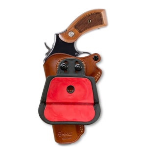 May include: A brown leather holster with a black plastic clip and a red rubber insert. The holster is designed to hold a revolver. The holster is made by MASC.