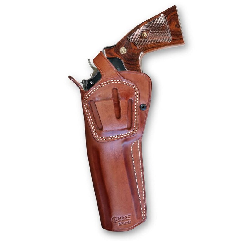 May include: A brown leather holster with white stitching for a revolver. The holster has a belt loop and a snap closure. The holster is made by MASC and is hand-made.