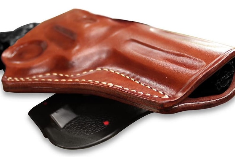 May include: A brown leather holster with white stitching. The holster is folded in half, showing the inside of the holster.