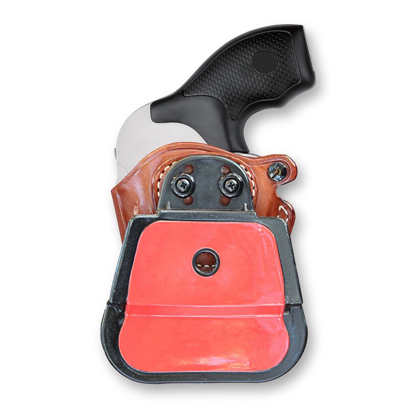 May include: A brown leather holster with a black plastic gun inside. The holster has a red plastic insert with a hole in the center. The gun has a black plastic handle with a textured surface.