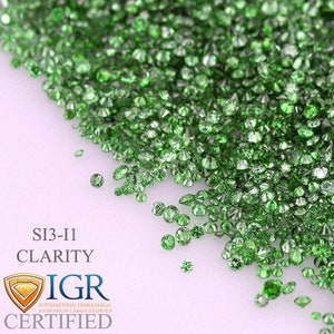May include: A collection of small, round, faceted green gemstones scattered on a white surface. The image includes text that reads "SI3-I1 CLARITY" and a logo that says "IGR CERTIFIED". The gemstones are a vibrant, light green color.