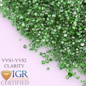 May include: A collection of small, round, faceted green gemstones scattered across a white surface. The image includes text that reads "VVS1-VVS2 CLARITY" and "IGR CERTIFIED" with a logo.