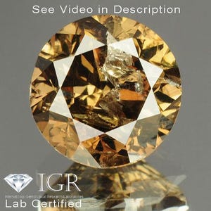 May include: A round, faceted gemstone with a warm, golden-brown hue. The gem has a complex, multi-faceted design with sharp angles and reflective surfaces. The image includes the text "See Video in Description" and the IGR Lab Certified logo.