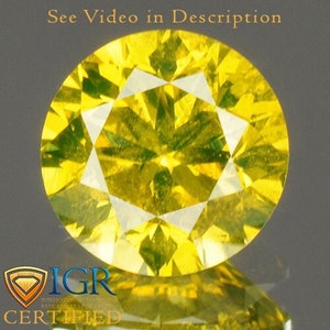 May include: A round, faceted yellow gemstone with a brilliant cut. The gem is set against a reflective surface, with the text "See Video in Description" at the top and the "IGR CERTIFIED" logo at the bottom.