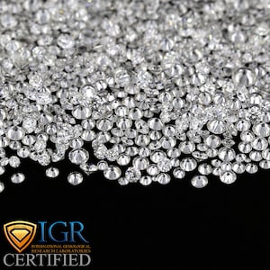 May include: A close-up shot of a collection of sparkling, round-cut diamonds. The diamonds are scattered across a black surface, creating a dazzling display of light and brilliance. The image includes the text "IGR CERTIFIED".