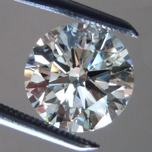 May include: A round-cut diamond held by tweezers. The diamond has many facets that reflect light, creating a sparkling effect. The gemstone appears colorless with hints of blue and yellow.