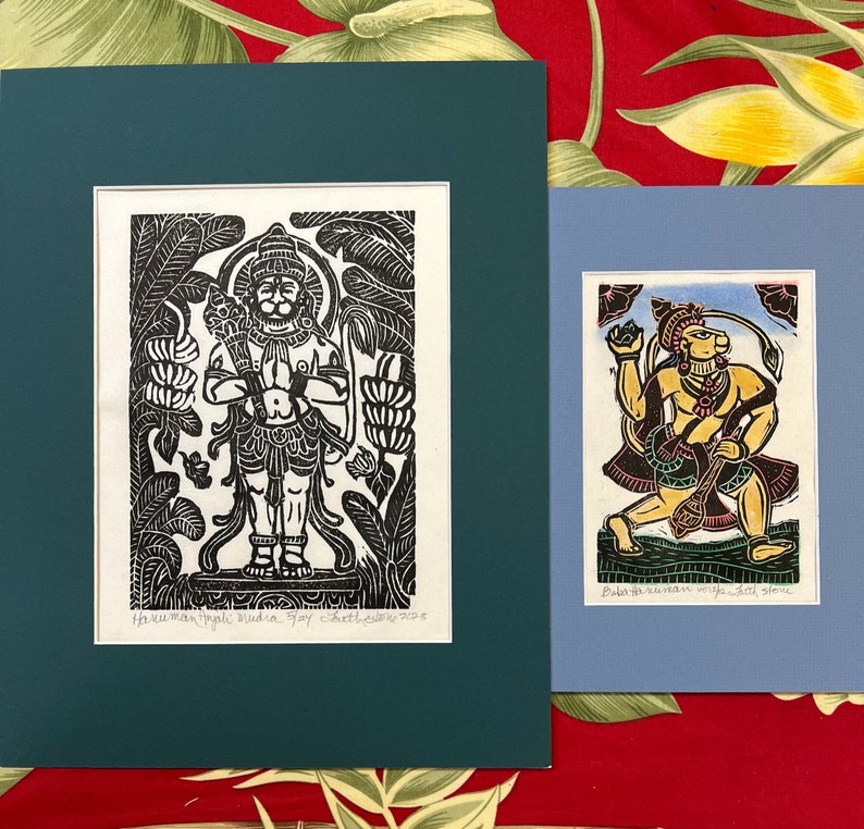 May include: Two framed black and white woodblock prints of Hindu deities. The print on the left depicts a standing figure with a crown and a third eye. The print on the right depicts a figure with a crown and a third eye holding a staff. The print on the left is titled "Hanumanthapali Buddha" and the print on the right is titled "Baba with Hanuman wife Sita & some"