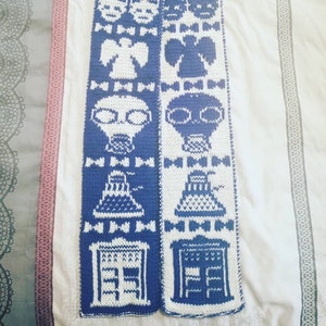May include: A blue and white knitted scarf with a repeating pattern of a spaceship, a face, and a bow tie. The scarf is made of a soft, fuzzy yarn.