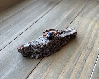 May include: A copper wire wrapped ring with a dark brown gemstone.