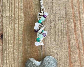 May include: A silver-toned DNA helix pendant necklace featuring small, round, multi-colored beads in shades of white, purple, and green, suspended from a delicate silver chain above a gray, heart-shaped stone.