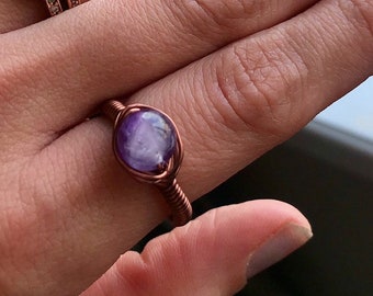 May include: A copper wire wrapped ring with a purple amethyst stone.
