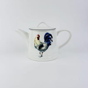 Könnte beinhalten: Eine weiße Keramik-Tasse mit schwarzem Henkel und dem Text "But First, Coffee" in schwarzer, fetter Schrift. Die Tasse steht auf einer weißen Oberfläche.