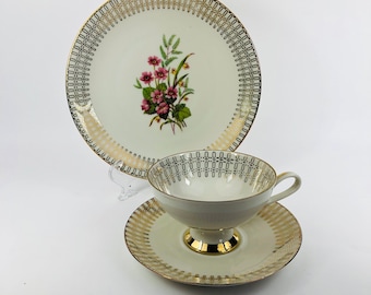 May include: A white teacup and saucer set with a gold and black geometric pattern. The saucer has a floral design with pink flowers.