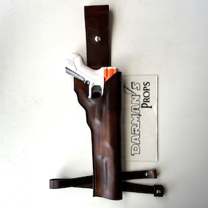 Könnte beinhalten: Ein braunes Lederholster mit einem Riemen und einer weißen Spielzeugpistole darin. Das Holster ist mit "Darman's Props" beschriftet.