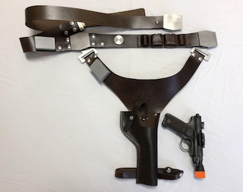 May include: A brown leather holster with a silver buckle and a black plastic toy gun. The holster is attached to a brown leather belt with silver buckles and a silver metal plate.