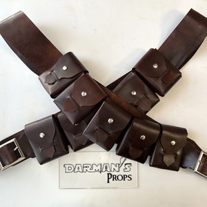 Puede incluir: Dos cinturones de cuero marrón con múltiples bolsas pequeñas adjuntas. Los cinturones están cruzados entre sí y tienen hebillas plateadas. El texto "Darman's Props" es visible en una etiqueta blanca.