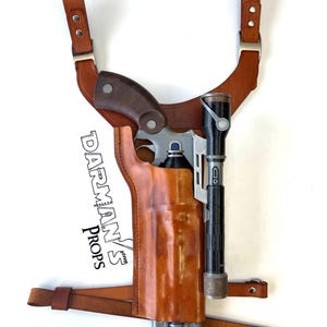 May include: A brown leather holster with a shoulder strap for a pistol and a flashlight. The holster is labelled "Darman's Props".