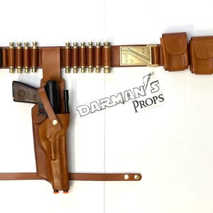 May include: A brown leather belt with a gold buckle and multiple pouches. The belt has a row of brass bullet casings attached to it. A brown leather holster with a gun is attached to the belt.