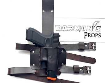May include: A dark brown leather shoulder holster with a black handgun and an orange magazine. The holster has adjustable straps and silver buckles. The text "DARMAN'S PROPS" is visible in the background.