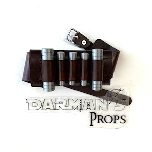 May include: A brown leather belt with a silver buckle and five silver cylindrical pouches attached. The belt is labeled "DARMAN'S PROPS".