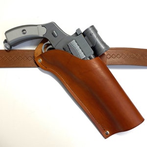 May include: A brown leather holster with a silver-colored pistol and flashlight attached. The holster has a belt loop and a snap closure.