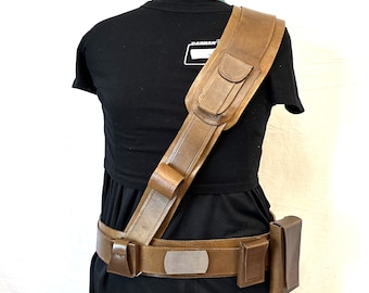 May include: A brown leather belt with a large buckle and a matching shoulder strap with a pocket. The strap is worn diagonally across the body.