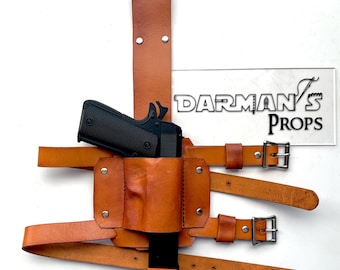 May include: A brown leather holster with a black handgun and two straps with buckles. The holster is designed to be worn on the thigh. The text "DARMAN'S PROPS" is visible in the background.